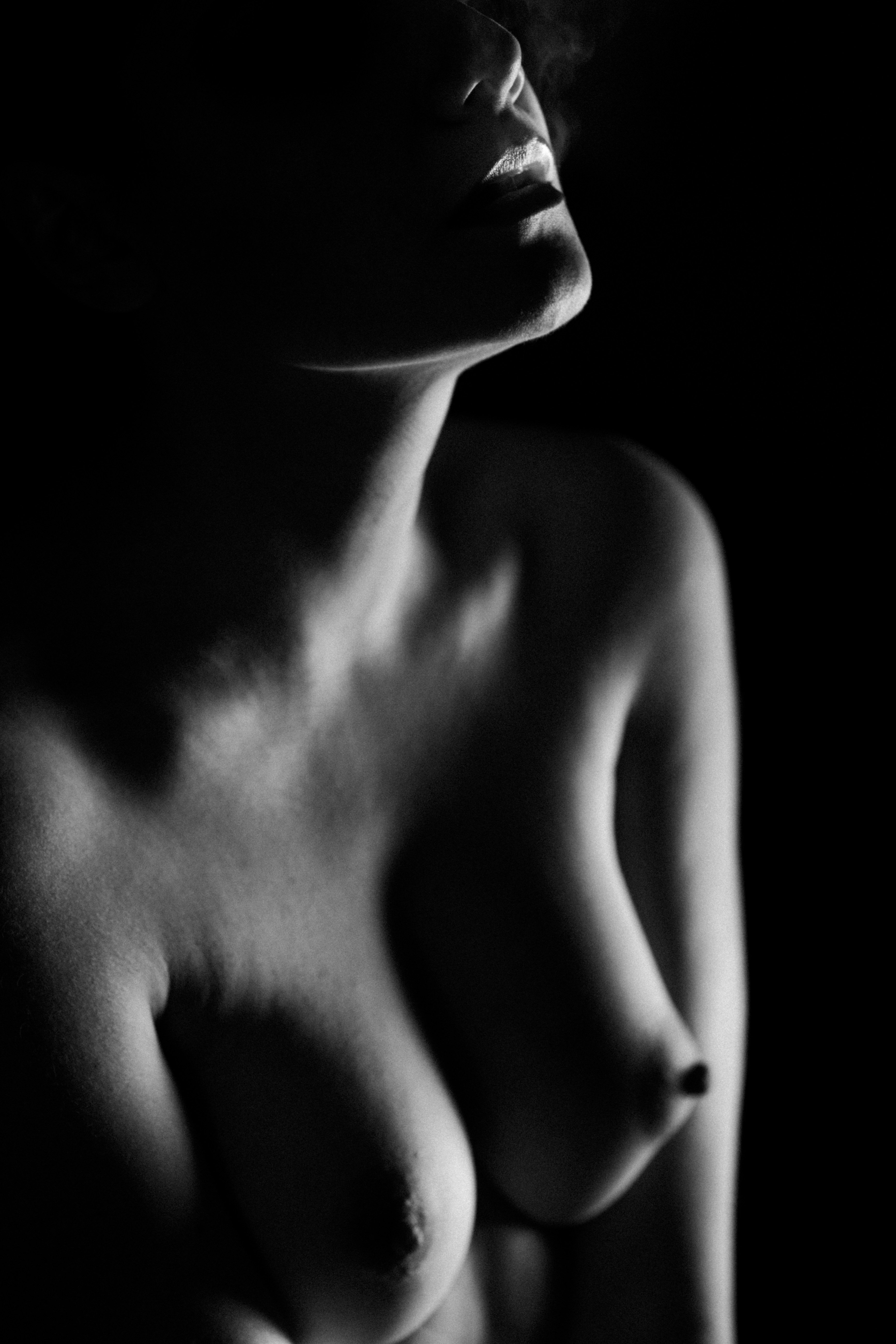 Dettaglio in bianco e nero del torace e delle clavicole di una donna; il volto è fuori inquadratura, seno e spalla illuminati di taglio, ombre profonde sullo sfondo.